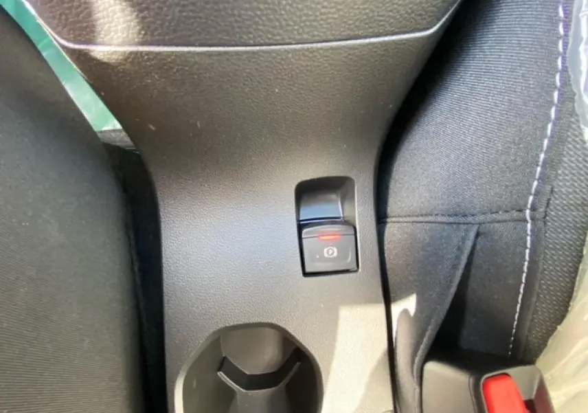 Gros plan sur le frein à main électrique et porte-gobelet entre les sièges noirs de la Dacia Logan gris 2022.