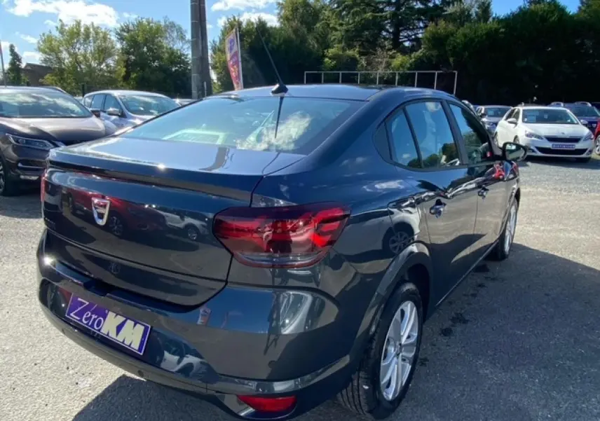 Vue 3/4 arrière droite d'une Dacia Logan gris métallisé 2022 avec feux arrière rouges et antenne de toit visible.