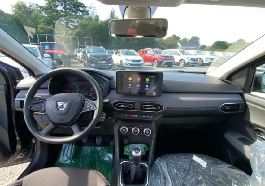 Intérieur de la Dacia Logan gris 2022, vue du poste de conduite avec volant, écran tactile et boîte manuelle visible.