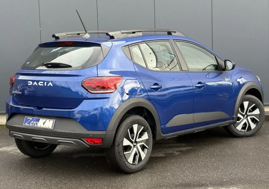 Vue 3/4 arrière droite d'une Dacia Sandero Stepway 2025 Bleu Iron avec barres de toit et jantes spécifiques.