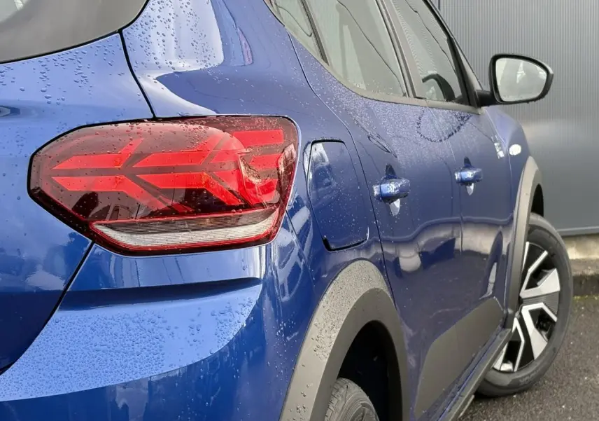 Vue 3/4 arrière droite d'une Dacia Sandero Stepway 2025 Bleu Iron avec feux arrière en Y et jantes spécifiques.