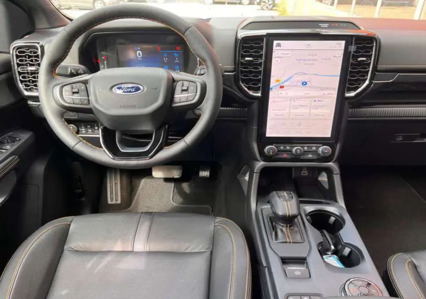 Vue intérieure du Ford Ranger 2025 Wildtrak Plus, tableau de bord avec écran tactile vertical et volant multifonction noir.
