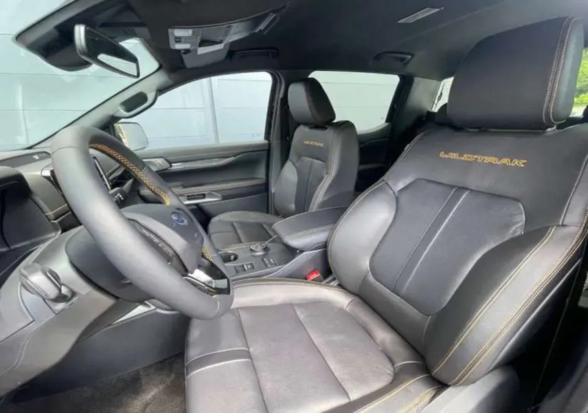 Vue intérieure côté conducteur du Ford Ranger 2025 Wildtrak Plus avec sièges cuir noirs et surpiqûres orange.