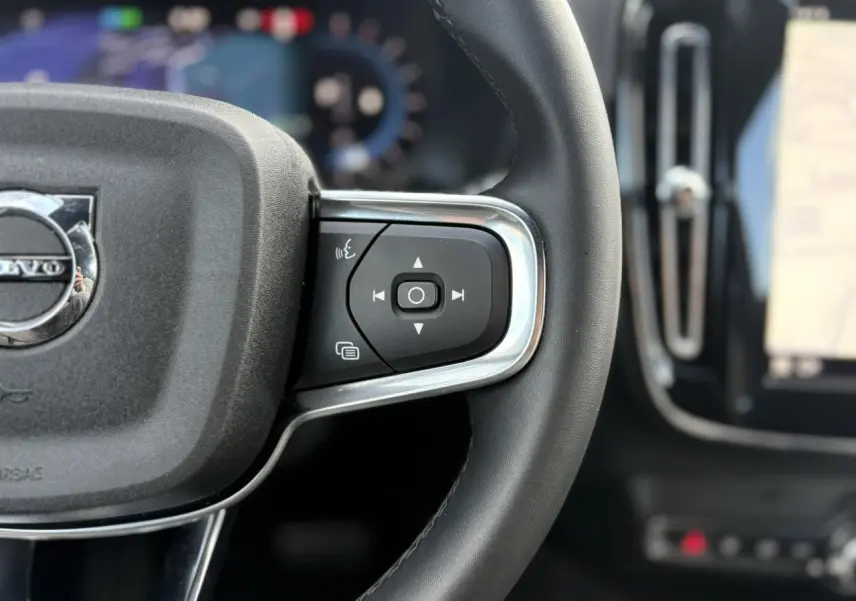 Gros plan sur le côté droit du volant noir du Volvo XC40 rouge Fusion 2024 avec commandes intégrées et logo central visible.