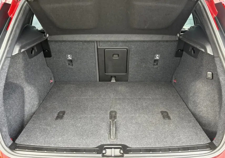 Coffre ouvert du Volvo XC40 B3 MHEV rouge Fusion, montrant l'espace de chargement et la moquette grise.