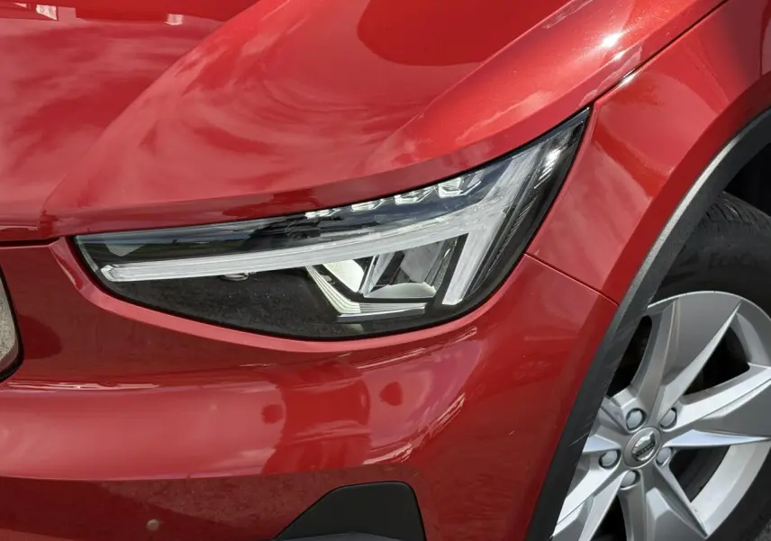 Gros plan sur le phare avant gauche et la roue alliage 18'' du Volvo XC40 rouge Fusion 2024.