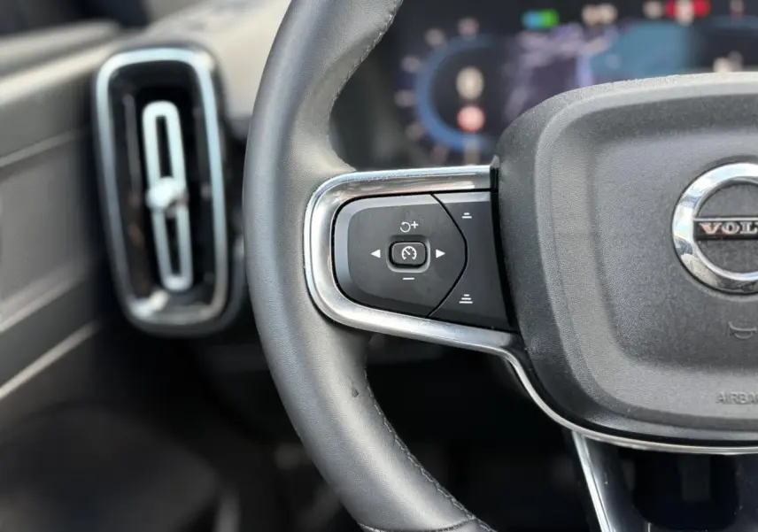 Gros plan sur la partie gauche du volant noir du Volvo XC40 2024 avec commandes de régulateur et aérateur vertical.