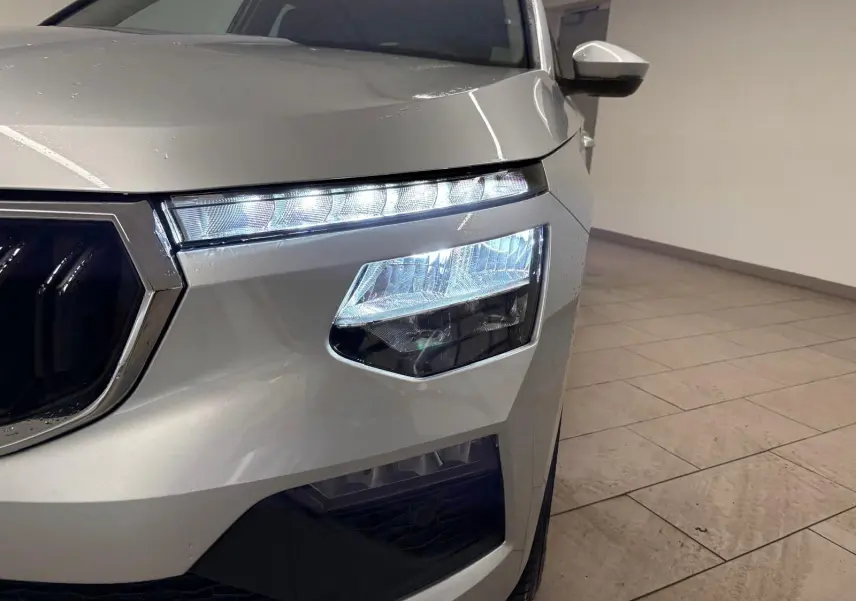 Gros plan sur le phare avant droit allumé du Skoda Kamiq gris argent, mettant en valeur les lignes modernes du SUV.