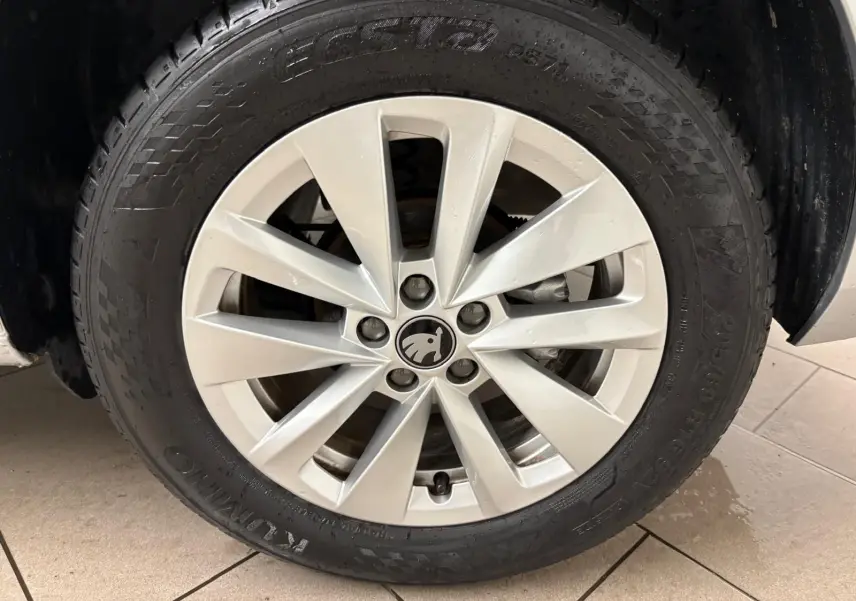 Gros plan sur la roue avant gauche avec jante argentée et logo ŠKODA au centre du SUV gris argent 2025.