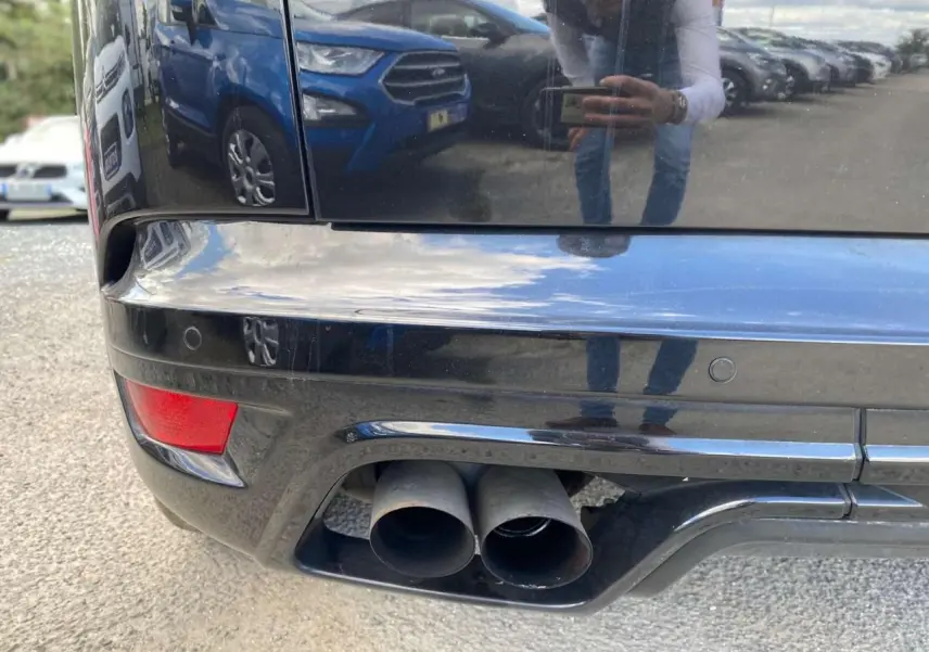 Gros plan sur la double sortie d’échappement arrière droite du Range Rover Sport noir, avec reflet du photographe sur la carrosserie.