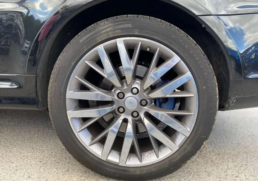Gros plan sur la jante 22 pouces argentée et l'étrier de frein bleu du Range Rover Sport noir côté gauche.