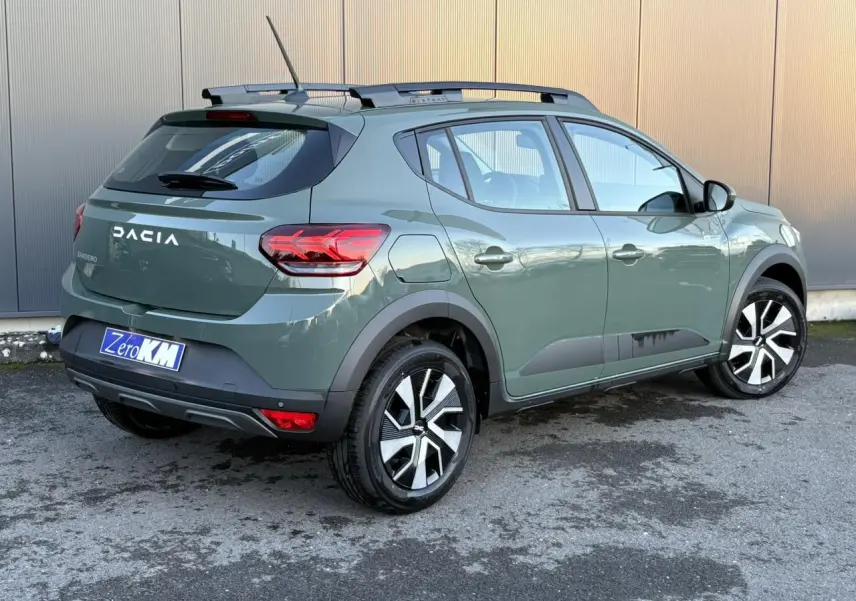 Vue 3/4 arrière droite d'une Dacia Sandero Stepway 2025 en kaki lichen avec barres de toit et jantes noires et argentées.
