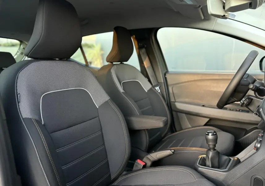 Vue intérieure côté conducteur de la Dacia Sandero Stepway 2025 avec sièges noirs et accoudoir central.