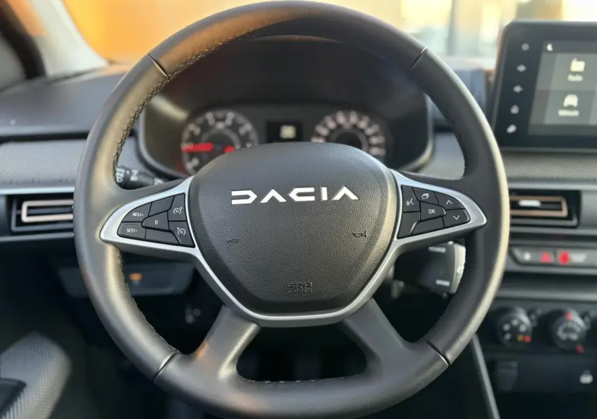 Volant noir en cuir avec logo Dacia au centre, tableau de bord et écran tactile du Dacia Sandero Stepway 2025 visibles en arrière-plan
