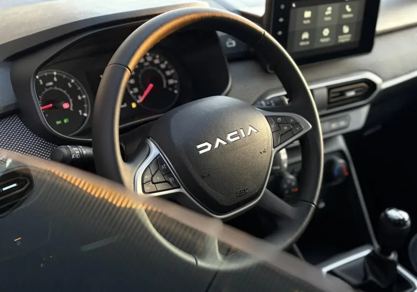 Vue rapprochée du volant noir Dacia avec commandes intégrées et tableau de bord numérique de la Sandero Stepway 2025.