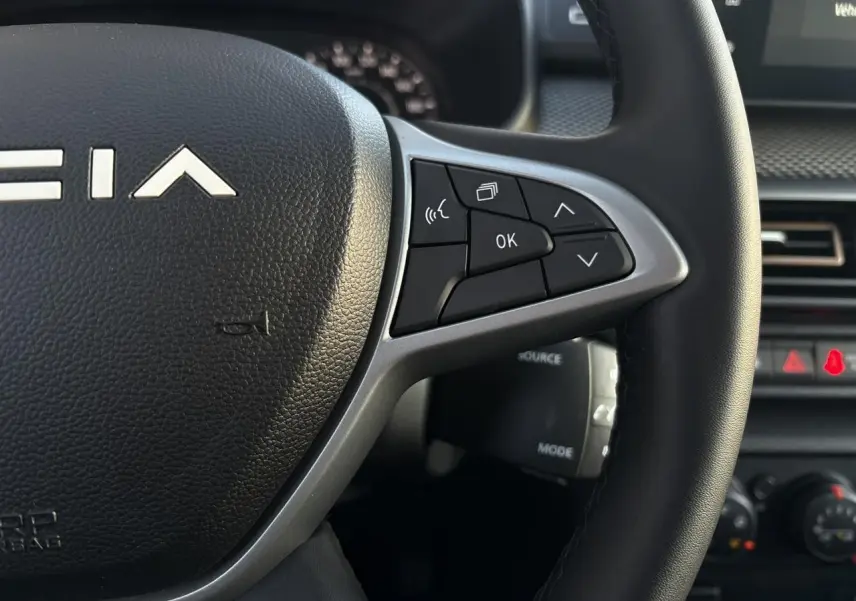 Gros plan sur le volant noir de la Dacia Sandero Stepway 2025 avec commandes multifonctions et logo central blanc.