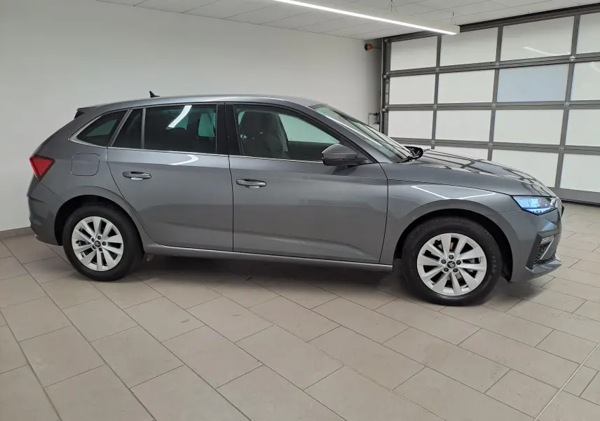 Vue latérale droite d'une Skoda Scala 2025 gris graphite métallisé, avec phares allumés dans un garage intérieur.