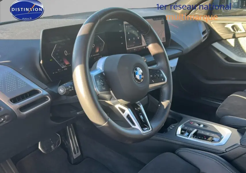 Vue intérieure côté conducteur du tableau de bord et volant de la BMW Série 1 118da 2025 en tissu noir avec coutures bleues.