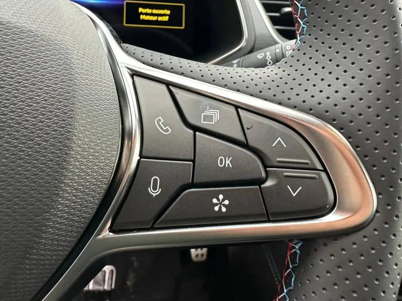 Gros plan sur les commandes au volant perforé du Renault Captur 2026 gris Rafale/Noir Étoilé, boutons multifonctions et surpiqûres tricolores.