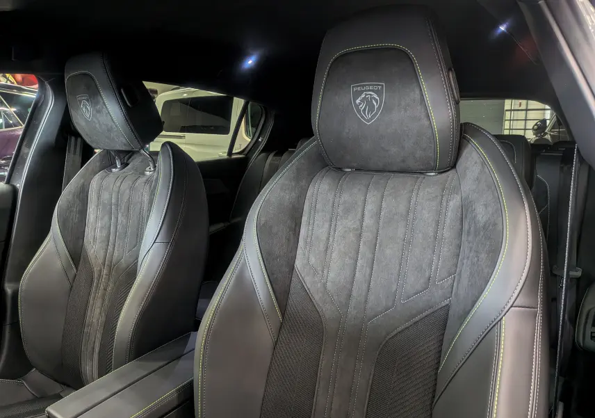 Gros plan sur les sièges avant en cuir noir et alcantara avec surpiqûres vertes et logo Peugeot embossé.