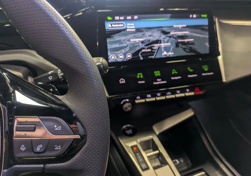Vue intérieure rapprochée du volant et de l’écran tactile central affichant la navigation dans une Peugeot 308 gris Sélénium 2026.