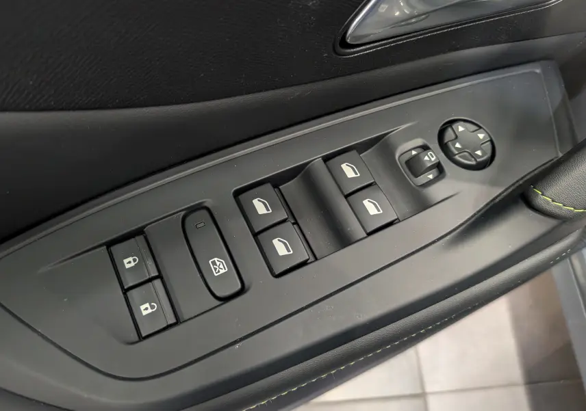 Gros plan sur les commandes de lève-vitres et rétroviseurs côté conducteur du Peugeot 308 GT Exclusive 2026 en intérieur noir.