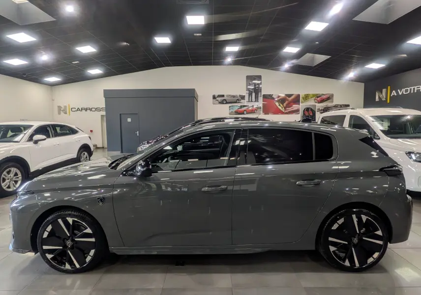 Peugeot 308 gris Sélénium vue de profil côté gauche, avec jantes noires et toit panoramique en intérieur showroom.