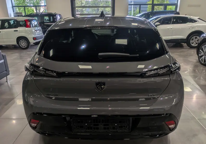 Vue arrière d'une Peugeot 308 GT Exclusive gris Sélénium, soulignant ses feux arrière étirés et son logo central noir brillant.