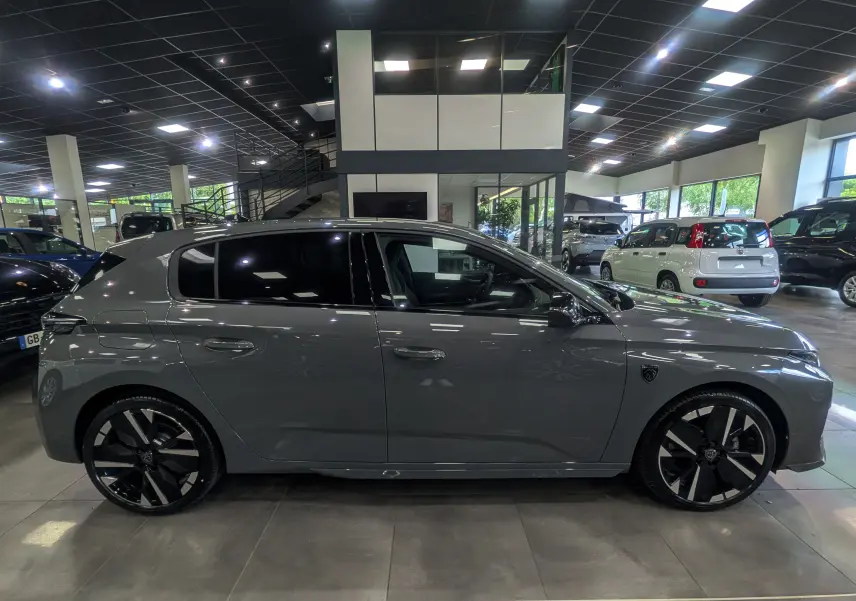 Vue de profil côté gauche d'une Peugeot 308 gris Sélénium avec jantes noires et toit noir dans un showroom.