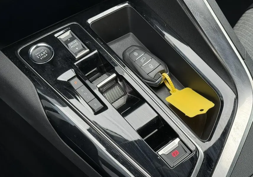 Vue rapprochée de la console centrale noire brillante du Peugeot 3008 Plug-in Hybrid avec clé et bouton start/stop.