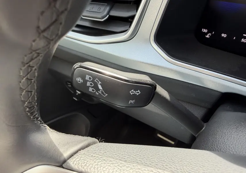 Gros plan sur la commande de clignotants et feux du Volkswagen T-Roc 2025, intérieur gris avec volant cuir noir.