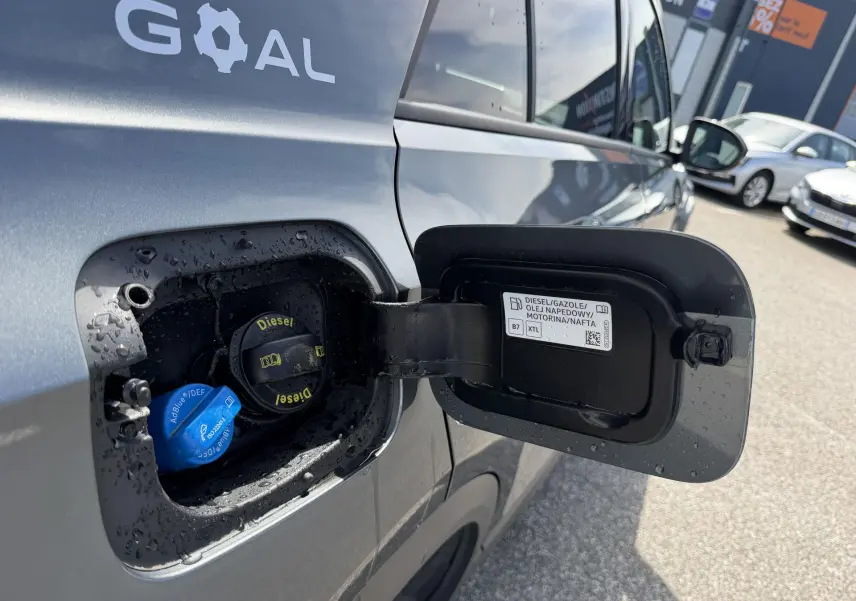 Vue rapprochée du côté gauche sur la trappe de carburant ouverte d’un Volkswagen T-Roc gris avec bouchons Diesel et AdBlue visibles.