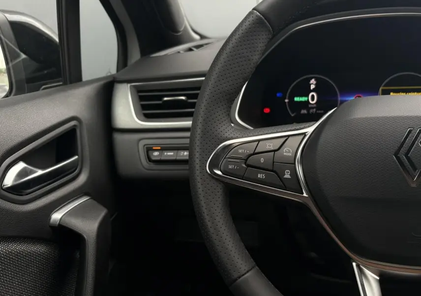 Gros plan sur le volant noir perforé et le tableau de bord numérique du Renault Captur hybride, côté conducteur.