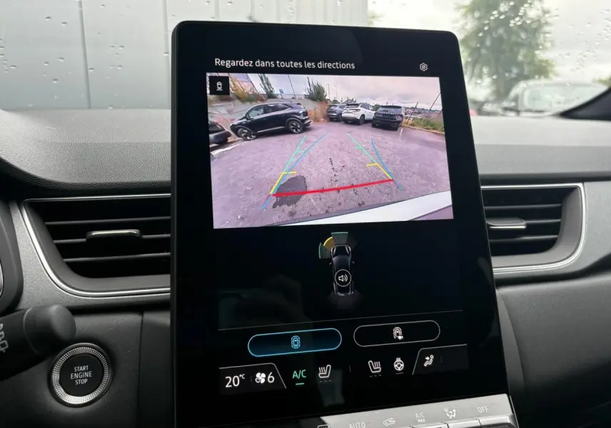 Vue intérieure du tableau de bord du Renault Captur blanc nacré, écran central affichant la caméra de recul et commandes climatisation.