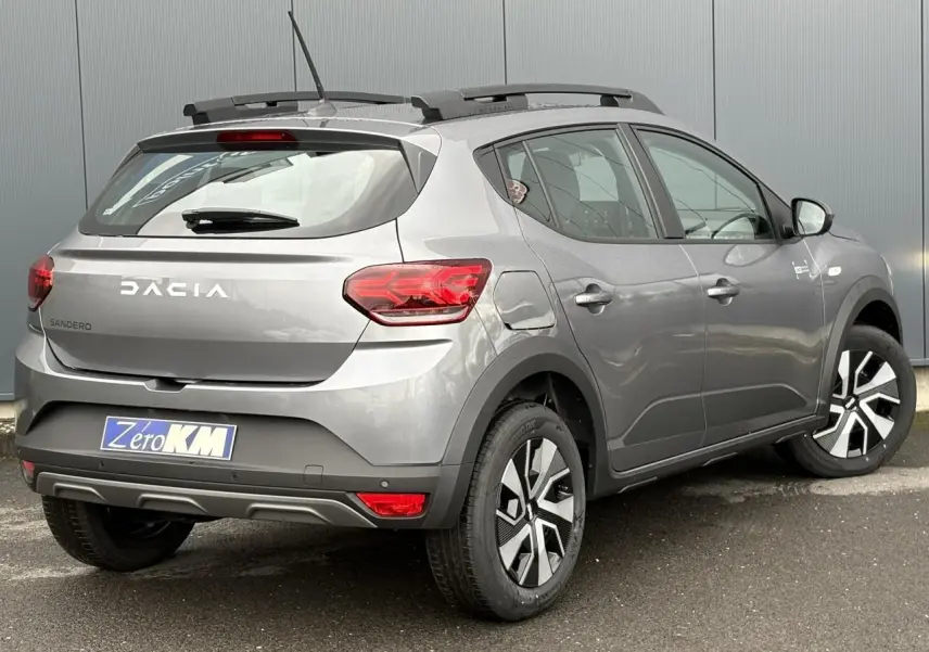 Vue 3/4 arrière droite d'une Dacia Sandero Stepway 2025 gris schiste avec barres de toit et jantes spécifiques.