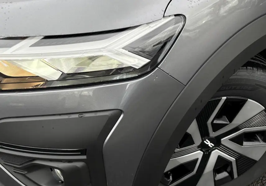 Gros plan sur le phare avant gauche et la roue avec enjoliveur noir et argent d'une Dacia Sandero Stepway gris schiste.