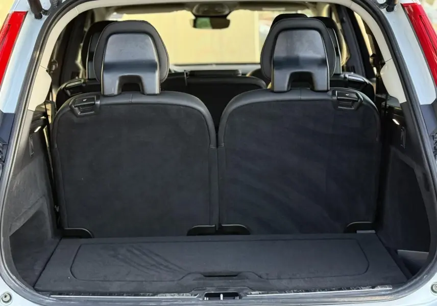 Coffre ouvert vu de l'arrière du Volvo XC90 blanc Crystal, montrant la troisième rangée de sièges noirs relevés.