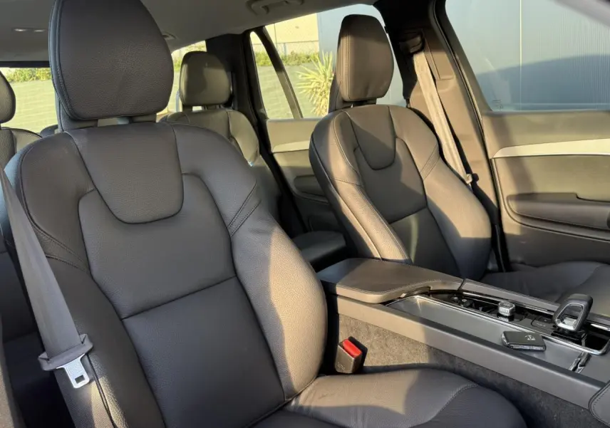 Vue intérieure sur les sièges avant en cuir noir du Volvo XC90 2024, avec accoudoir central et console moderne.