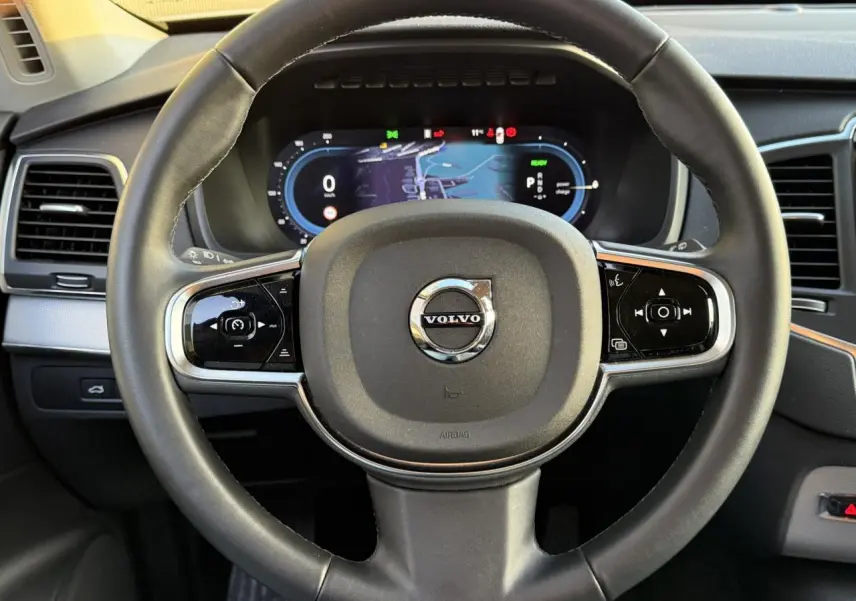 Vue rapprochée du volant noir de la Volvo XC90 2024 avec tableau de bord digital et commandes intégrées.
