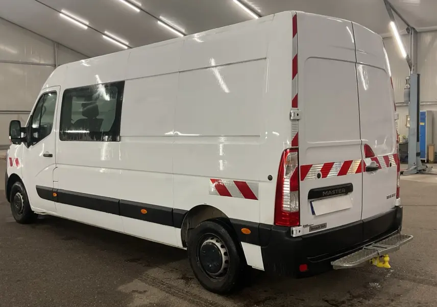 Vue 3/4 arrière droite d’un Renault Master blanc avec marquages réfléchissants rouges et blancs en intérieur d’atelier.