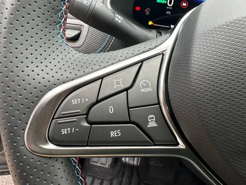 Gros plan sur les commandes noires du volant perforé du Renault Captur 2026 Gris Cassiopée/Noir Étoilé, avec surpiqûres bleues et rouges.