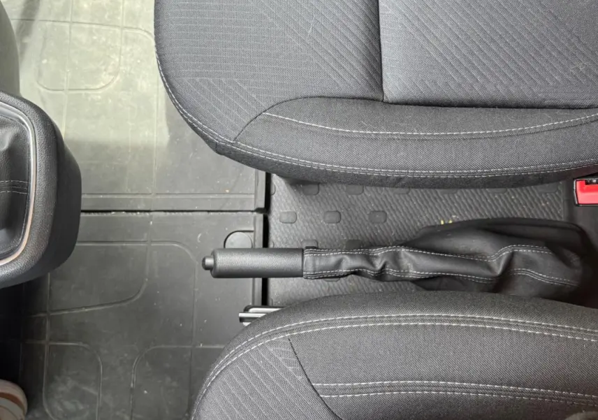Vue rapprochée de la poignée de frein à main entre les sièges avant gris foncé du Renault Trafic Fourgon 2024.