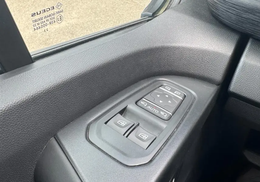 Gros plan sur les commandes électriques des vitres et rétroviseurs côté conducteur du Renault Trafic Fourgon gris foncé.