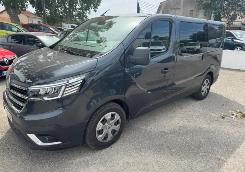 Renault Trafic Fourgon gris foncé en 3/4 avant droit, avec vitres surteintées et porte latérale visible.