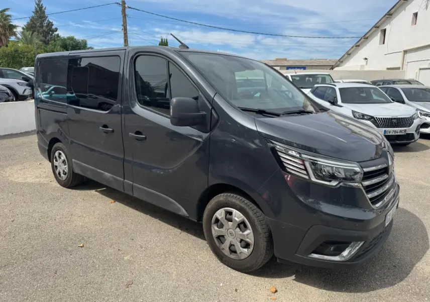 Renault Trafic Fourgon gris foncé en 3/4 avant droit, avec vitres surteintées et porte latérale visible.