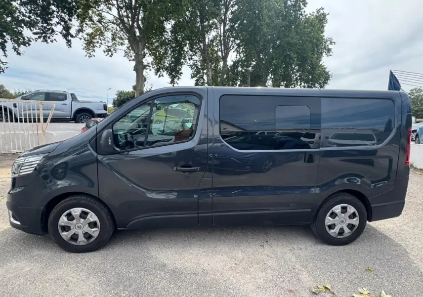 Profil côté gauche d'un Renault Trafic Fourgon gris foncé avec porte latérale et vitres surteintées.