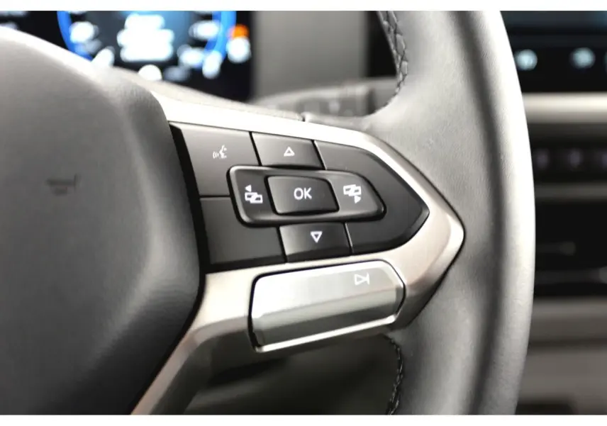 Gros plan sur les commandes multifonctions du volant en similicuir du Volkswagen Transporter gris Stone 2025.