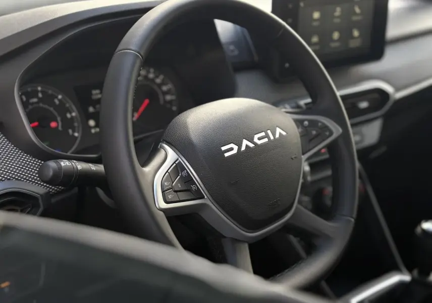 Gros plan sur le volant noir de la Dacia Sandero Stepway 2025 avec tableau de bord et écran tactile en arrière-plan.