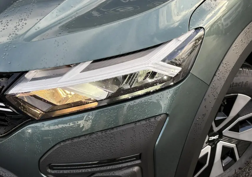 Gros plan sur le phare avant droit et la roue de la Dacia Sandero Stepway 2025 en Vert Cèdre métallisé.