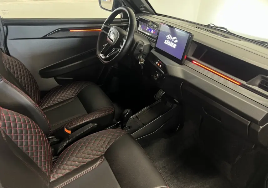 Vue intérieure côté conducteur de la Ligier JS50 bleu, avec sièges noirs à surpiqûres rouges et écran tactile central.